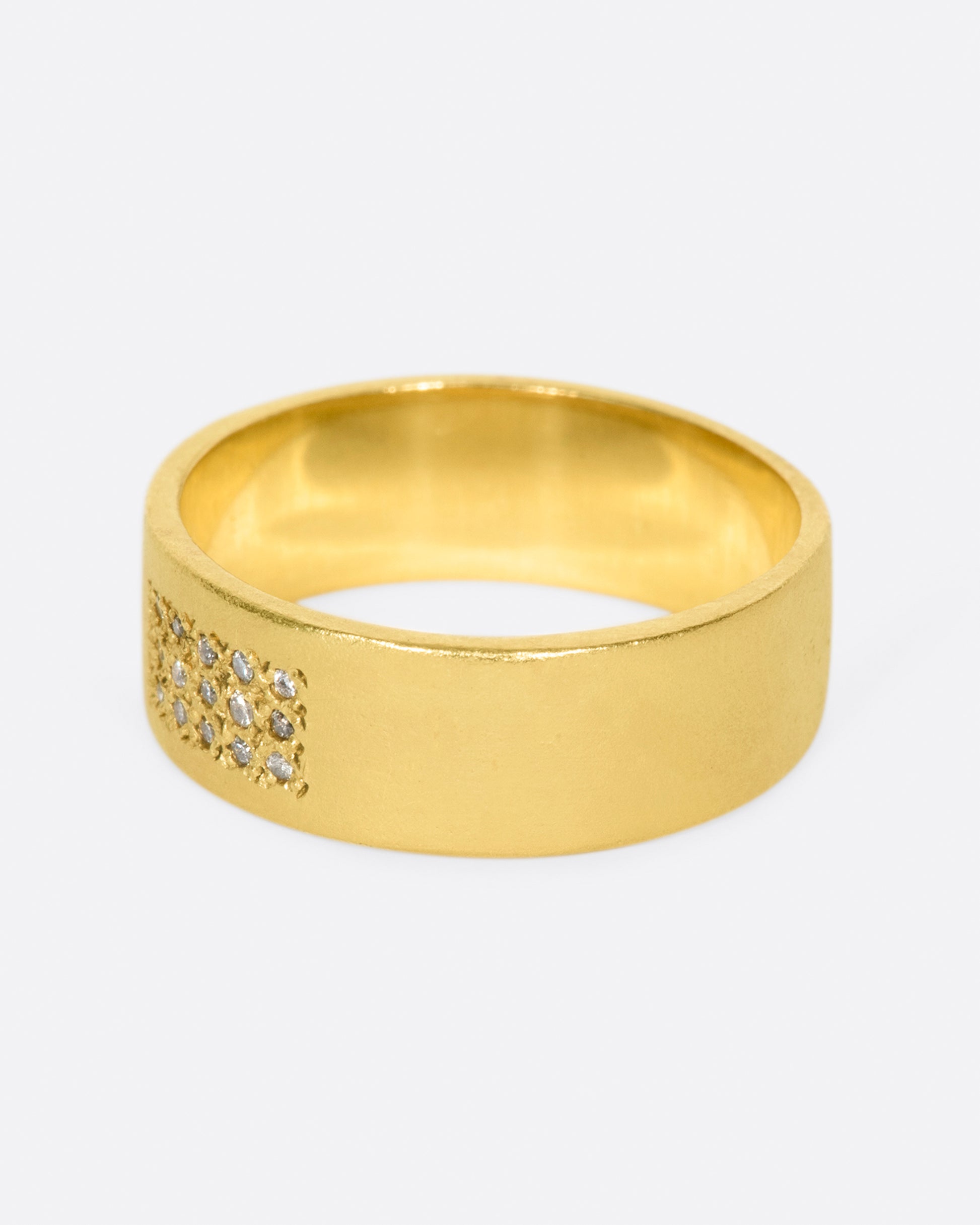 A yellow gold band with 15 grey diamonds in three rows of five at the center. Shown from the side.