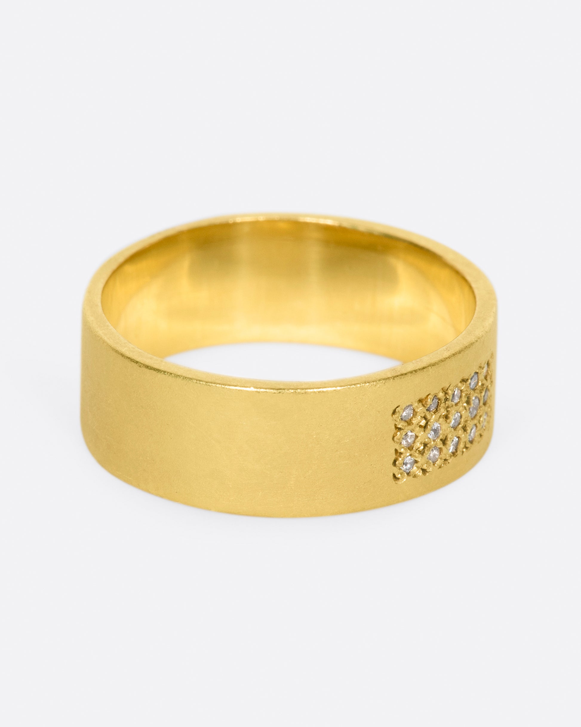 A yellow gold band with 15 grey diamonds in three rows of five at the center. Shown from the side.