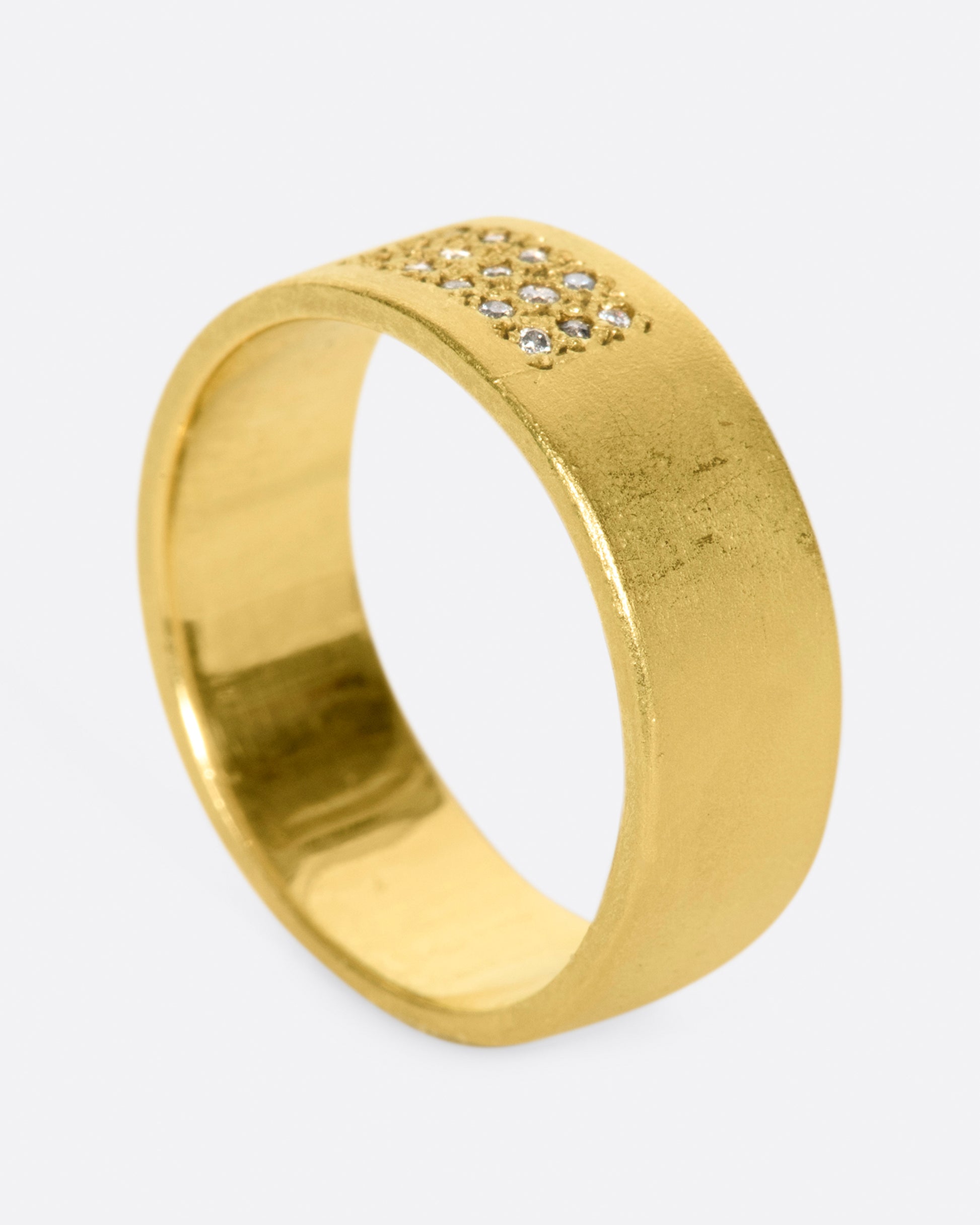 A yellow gold band with 15 grey diamonds in three rows of five at the center. Shown standing up from the side.