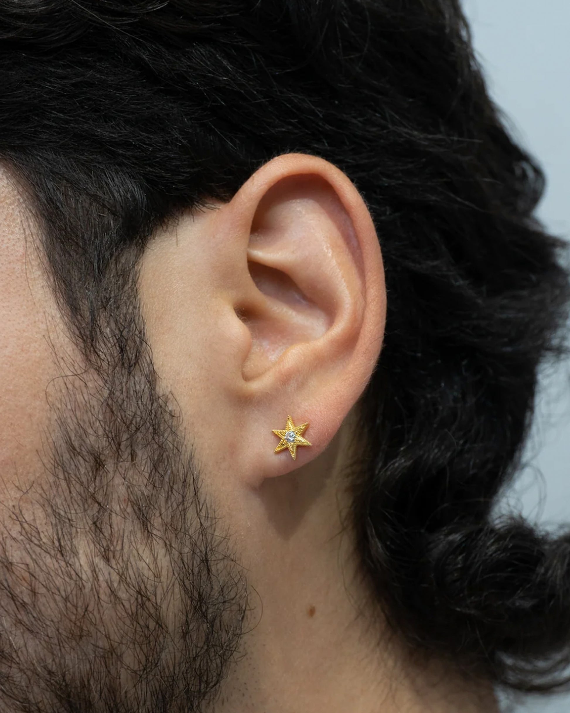 A six point star with millgrain texture and a bright white diamond center. Shown from the front on a person.