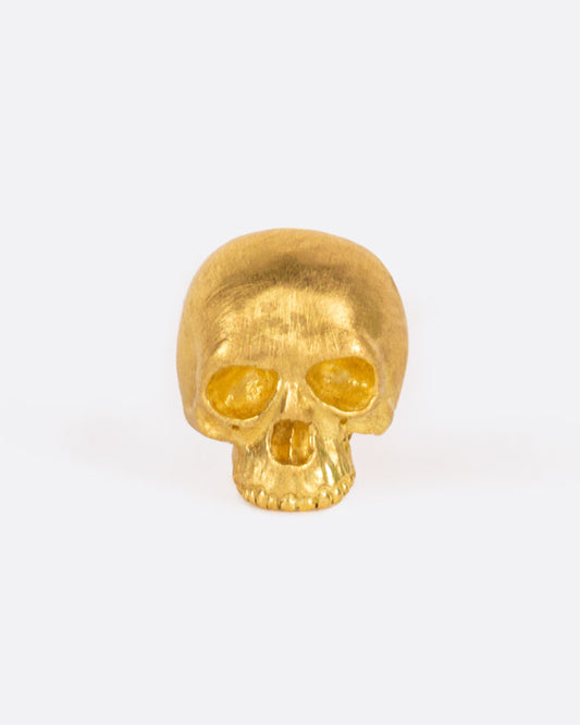 A solid yellow gold skull stud earring. Shown from the front.