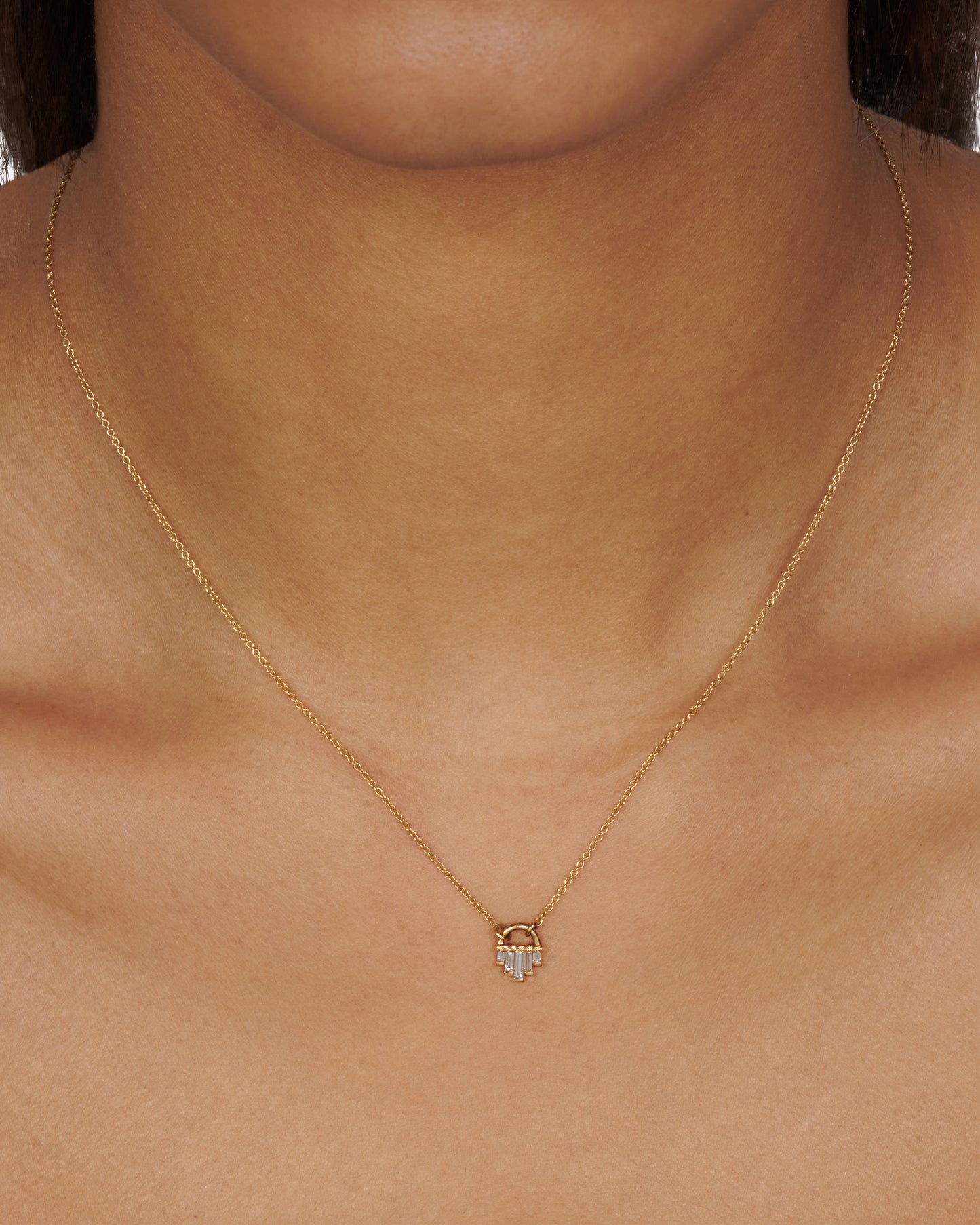 A curved gold pendant necklace with five diamond baguettes.