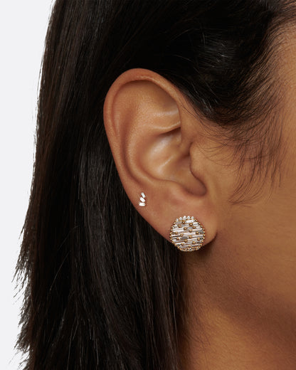 A round yellow gold, slightly concave stud earring covered in baguette diamonds, shown on a person.