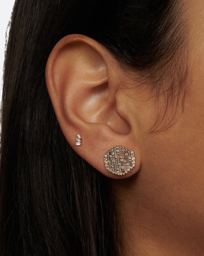 A round yellow gold, slightly concave stud earring covered in baguette diamonds, shown on a person.