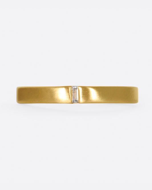 A matte gold band cast in a simple silhouette, featuring one needle baguette-cut diamond for that extra flare.