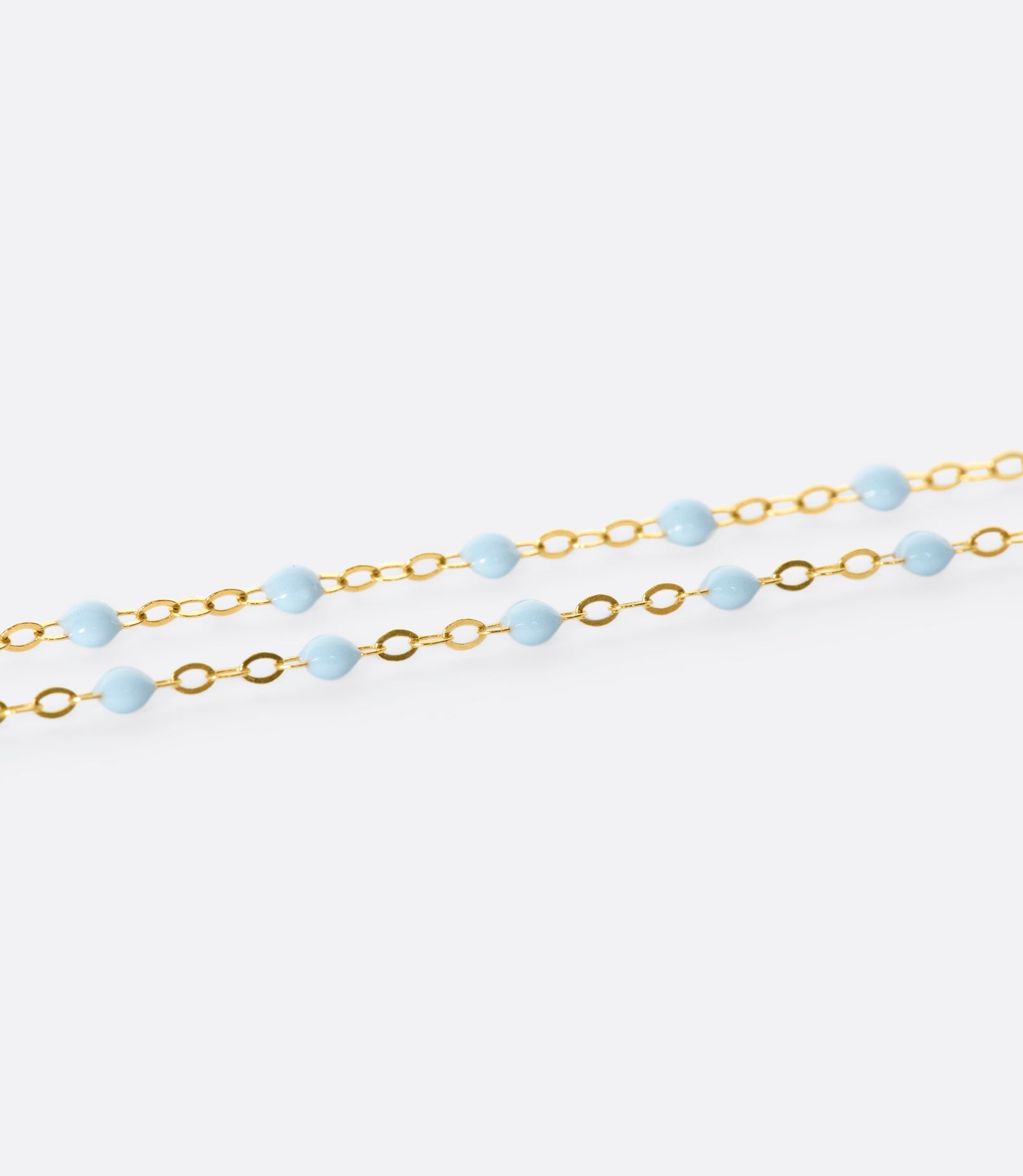 A close up view of a yellow gold cable chain necklace with baby blue resin droplets. Shown from the side.
