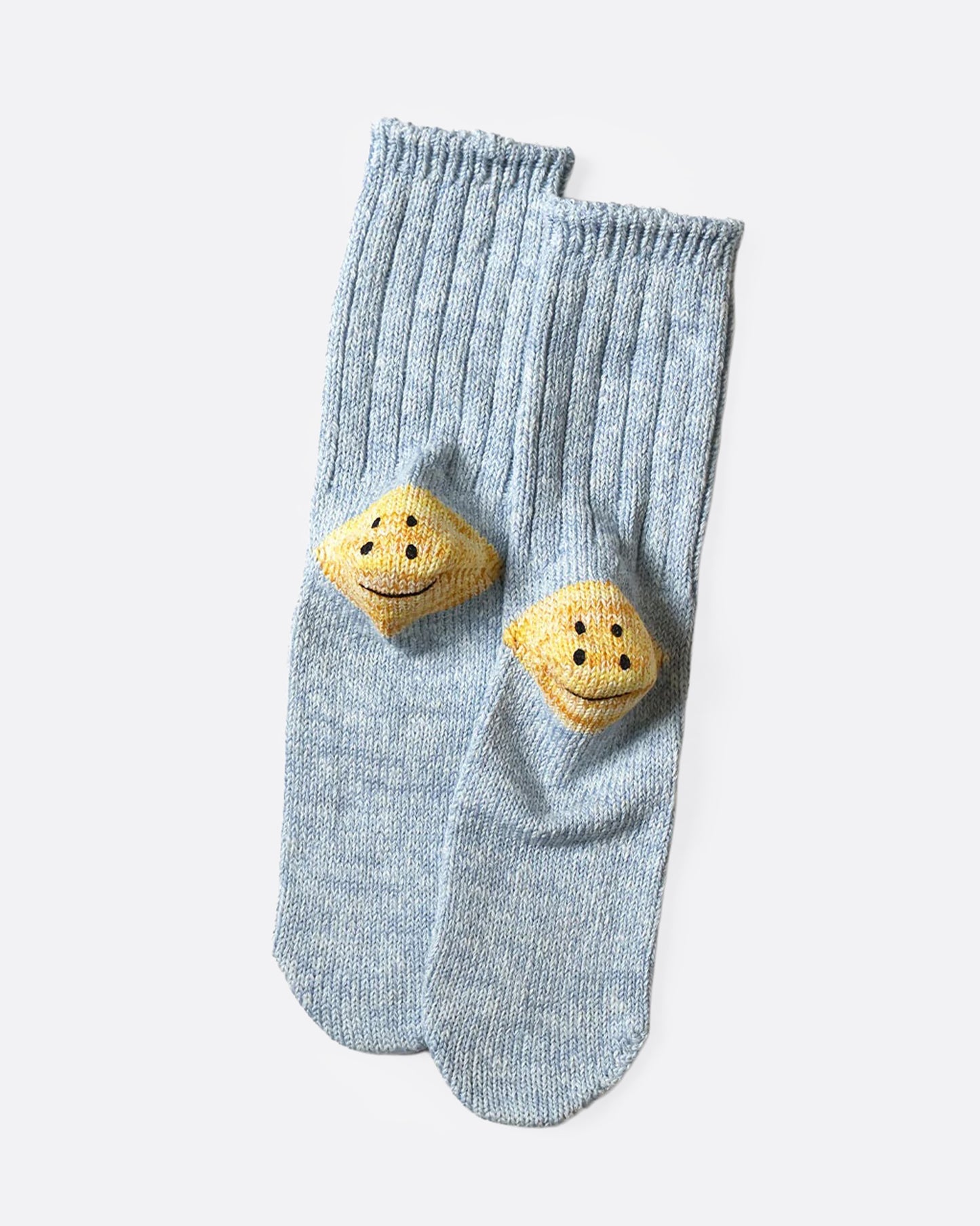 A pair of blue ribbed cotton socks with double-eyed smiley faces on each heel, shown from the bottom.