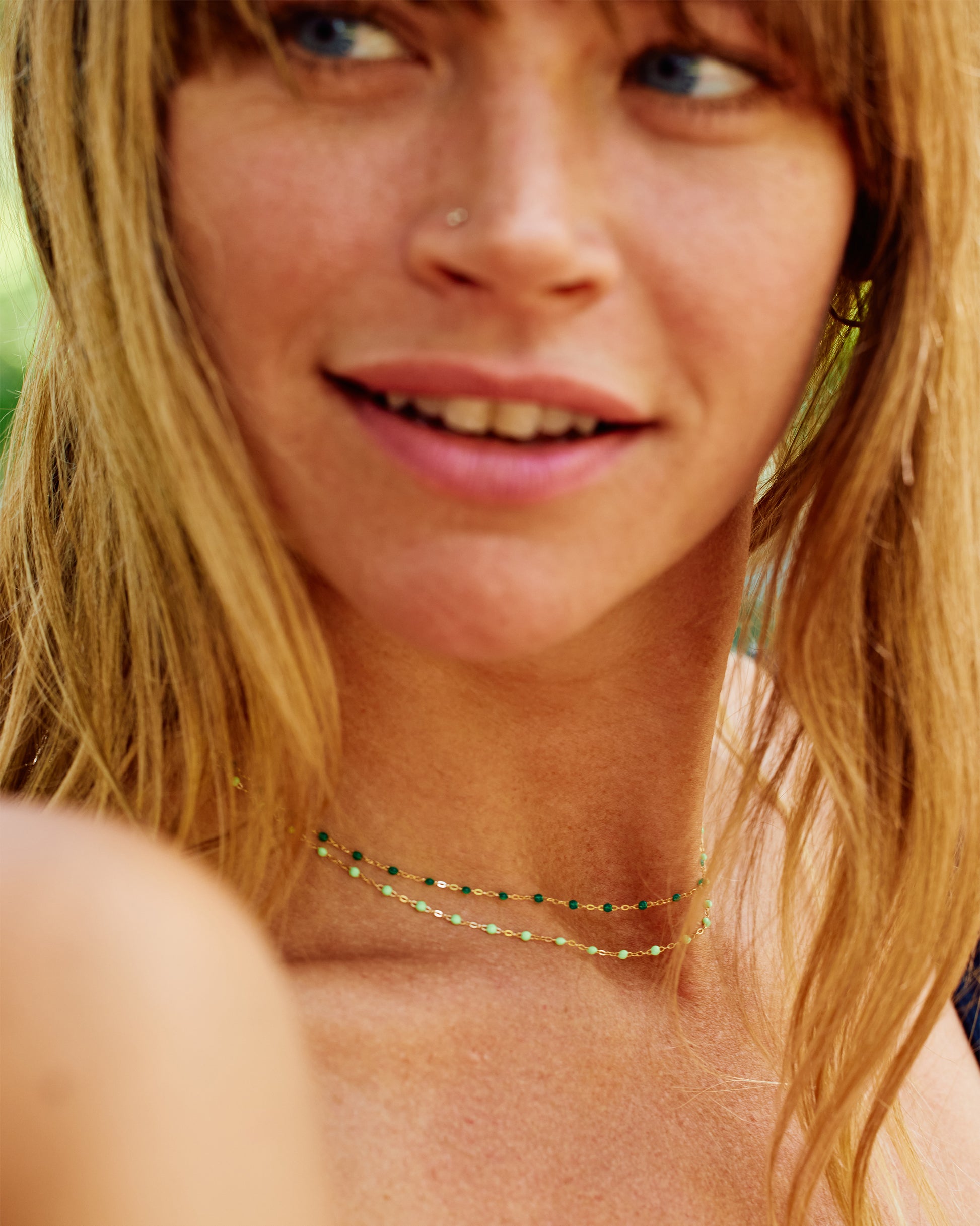 Two yellow gold cable chain necklaces shown from the side layered on a person. The bottom one has light green resin droplets, and the top one has dark green resin droplets. 