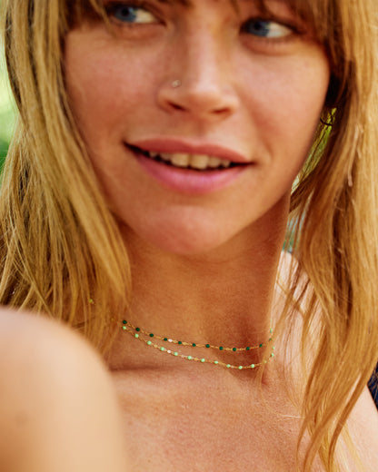 Two yellow gold cable chain necklaces shown from the side layered on a person. The bottom one has light green resin droplets, and the top one has dark green resin droplets. 