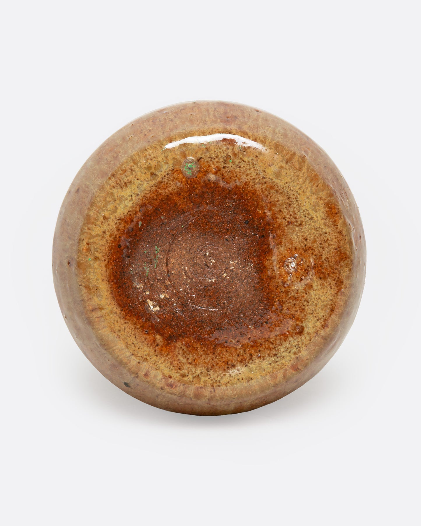 A tan ceramic vase with a dripped umber glaze, shown from the bottom.