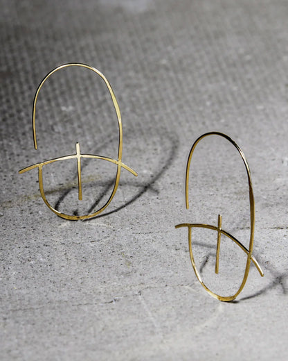 Gold wire oval hoop earrings, the pair standing on stone, casting shadows