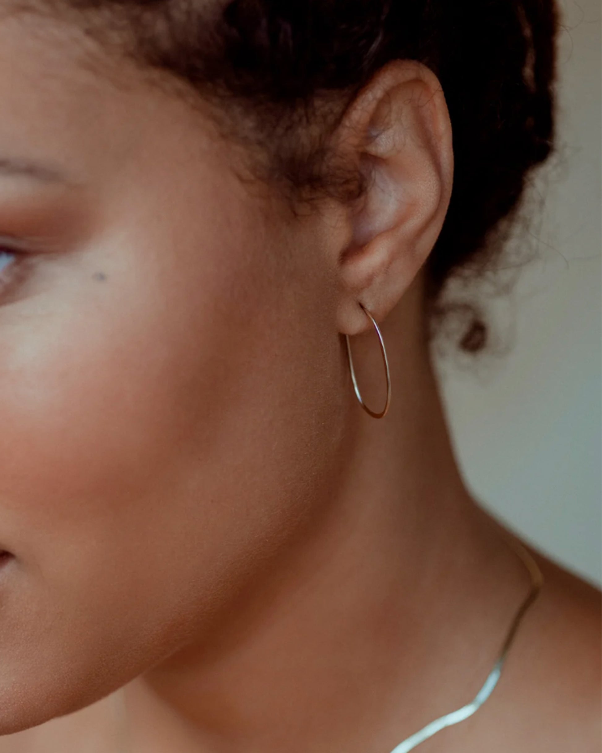 A pair of yellow gold, oval, hammered wire hoops with a hook closure, shown on an ear.