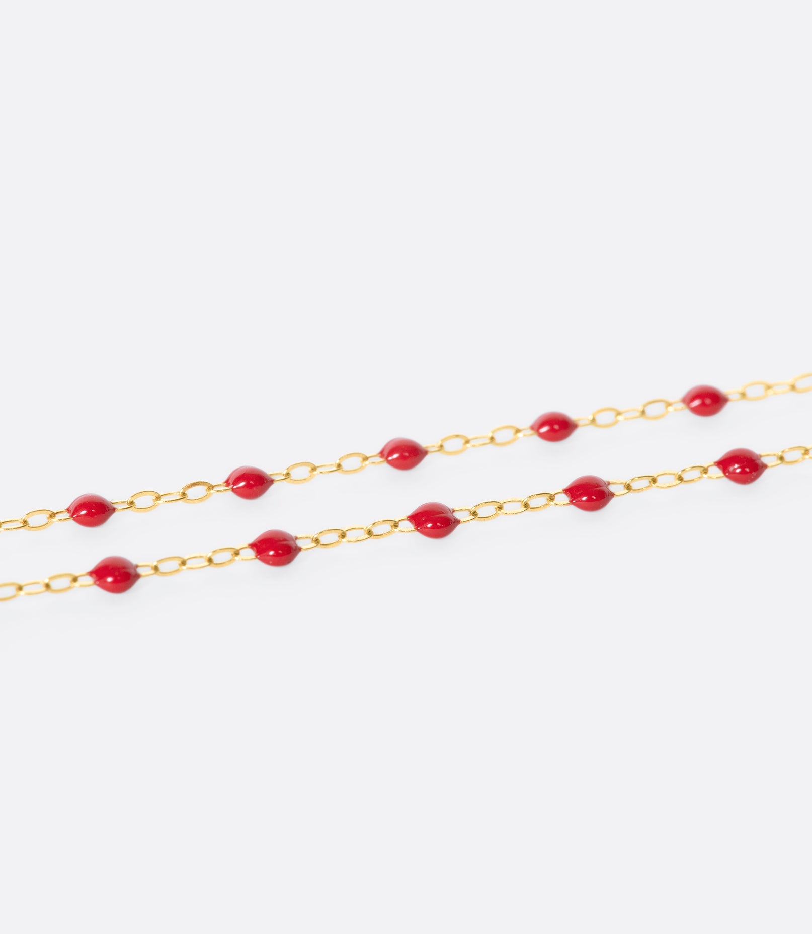 A close up view of a yellow gold cable chain necklace with red resin droplets. Shown from the side.