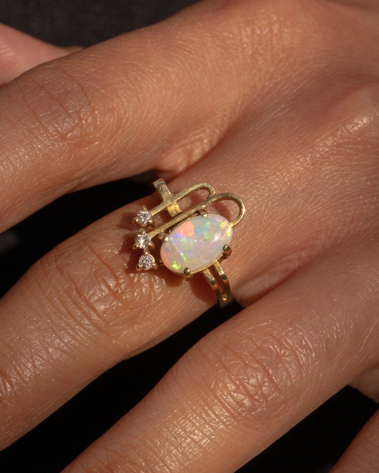 A yellow gold ring with a trio of diamonds, two Deco- inspired arches, and a prong set opal. Shown worn.