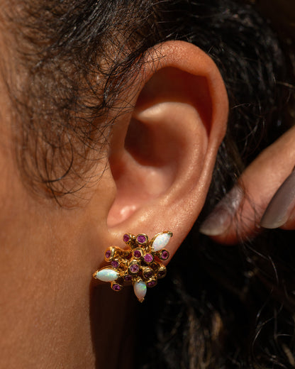 A yellow gold starburst stud earring with pink sapphires and opals, shown on a person.