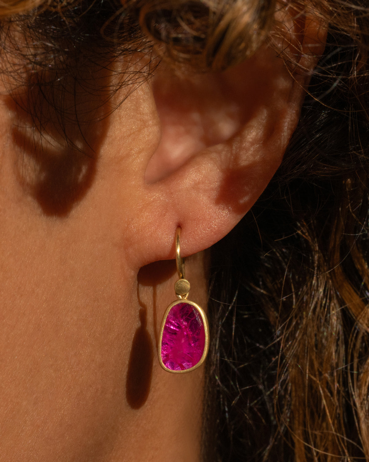 Lola Brooks earring in 18k yellow gold worn on an ear, a faceted Mozambique ruby pebble in a gold bezel on a hook wire