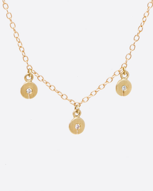 A yellow gold cable chain necklace with three disc charms. Each disc has a single gray diamond with a slit in the bottom. Shown from the front.