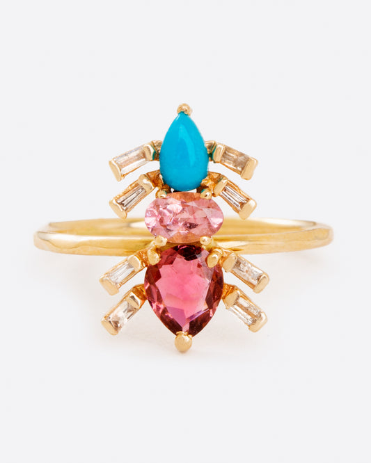 A yellow gold ring with pink tourmalines, turquoise, and baguette diamonds in the shape of an ant. Shown from the front.