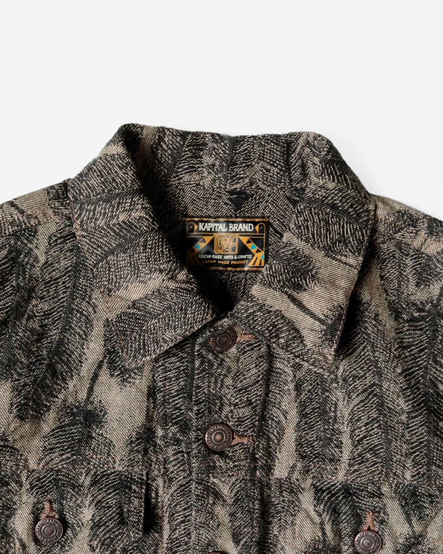 A close up of a black and beige jacquard denim jacket with an all-over 3D feather motif and a cut-off hemline and raw feathered seam. Shown from the front.
