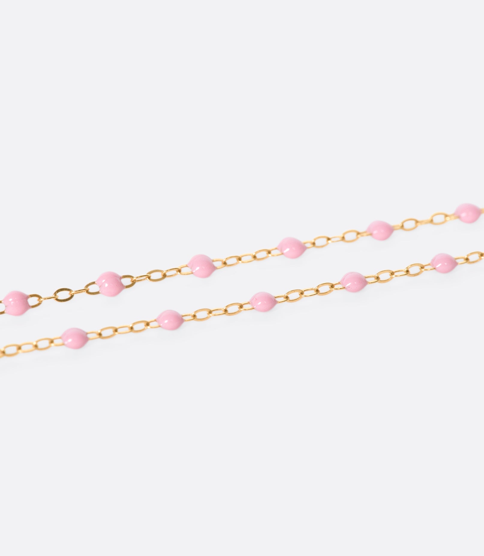 A close up view of a yellow gold cable chain necklace with pink resin droplets. Shown from the side.