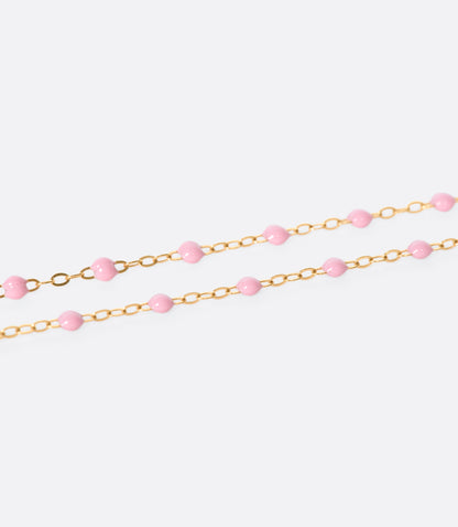 A close up view of a yellow gold cable chain necklace with pink resin droplets. Shown from the side.