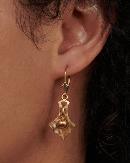 Vintage yellow gold fan drop earrings worn on an ear