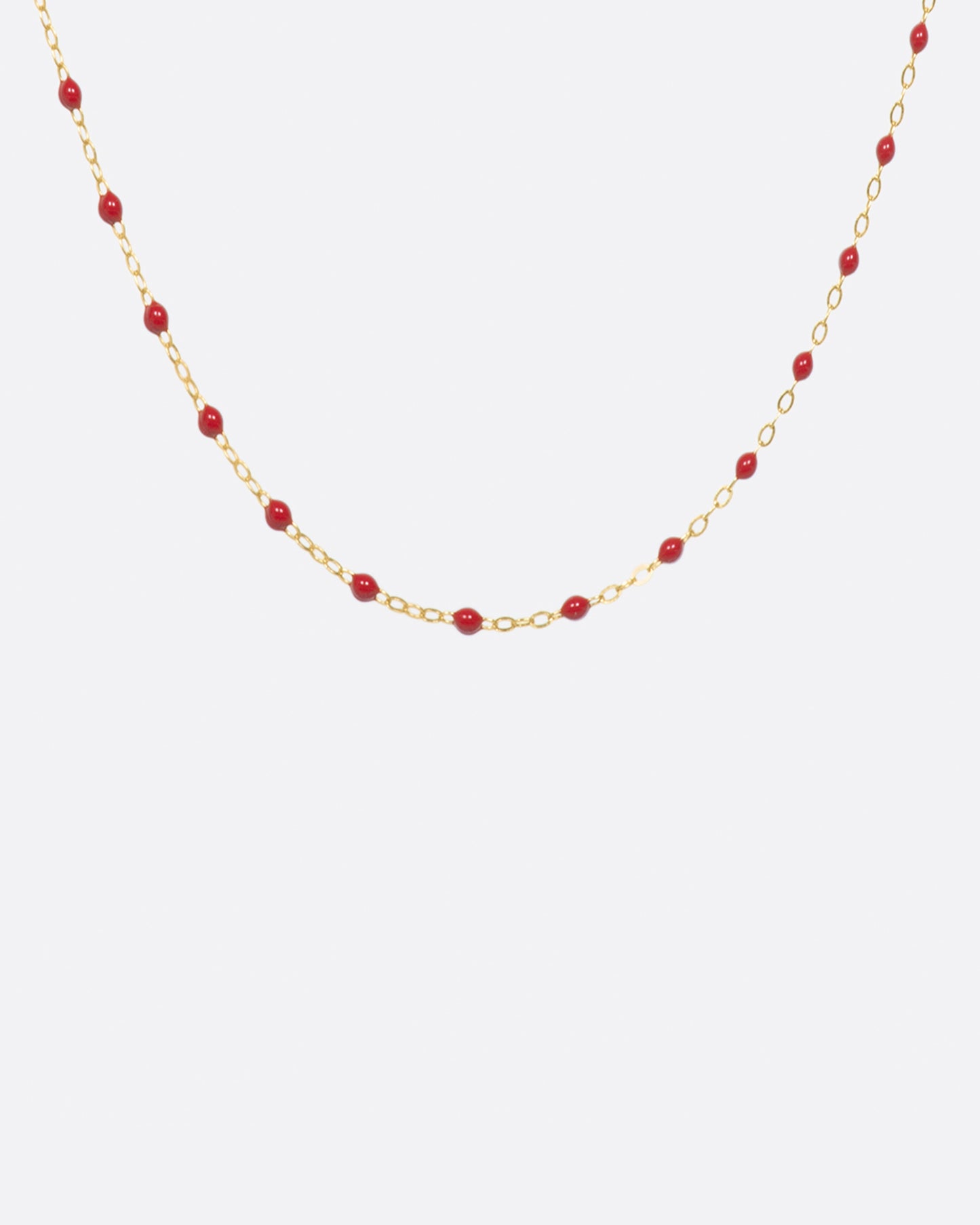 A yellow gold cable chain necklace with droplets of red resin. Shown from the front.