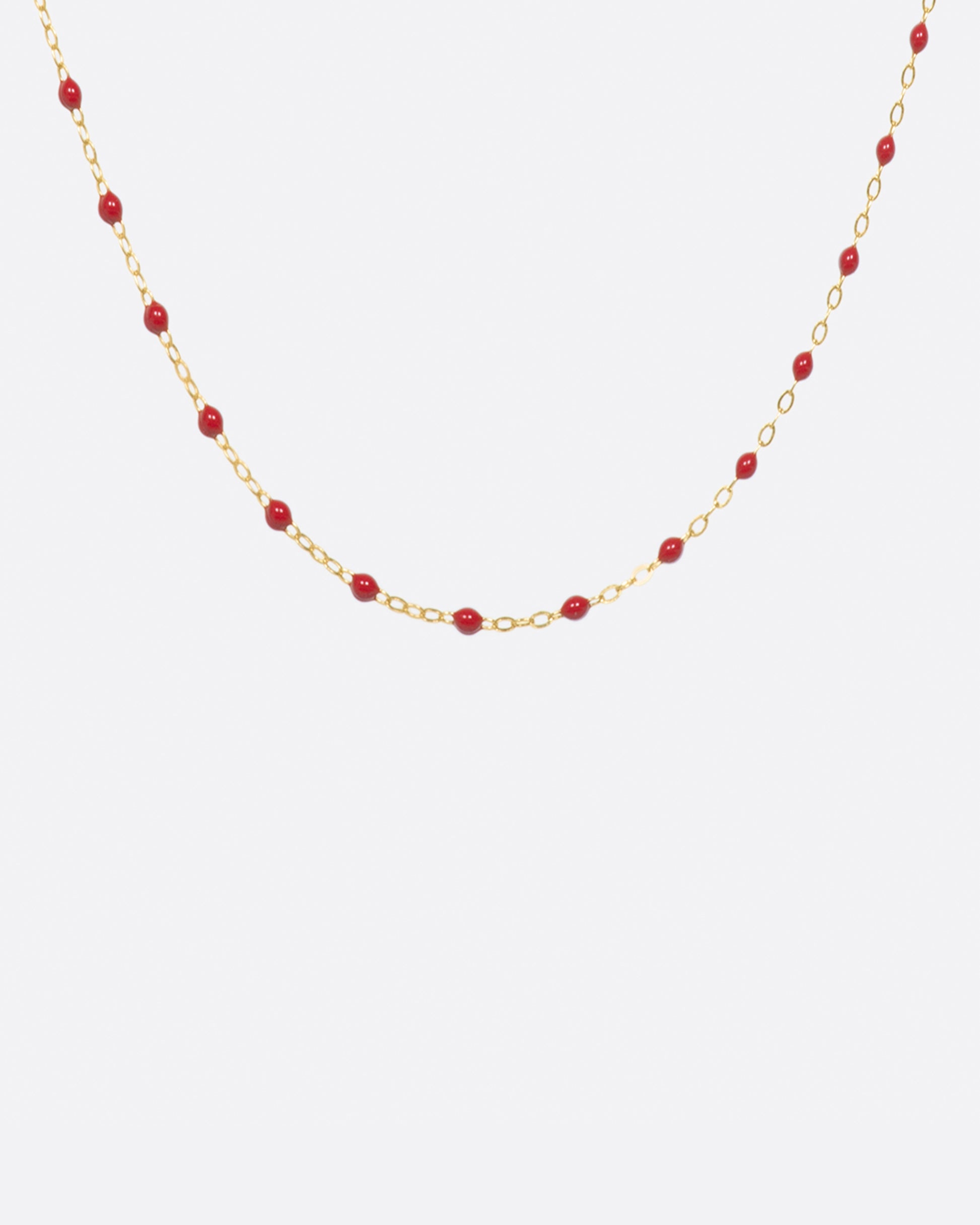 A yellow gold cable chain necklace with droplets of red resin. Shown from the front.