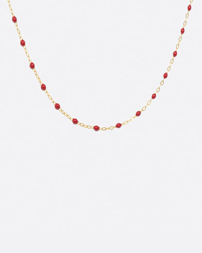 A yellow gold cable chain necklace with droplets of red resin. Shown from the front.