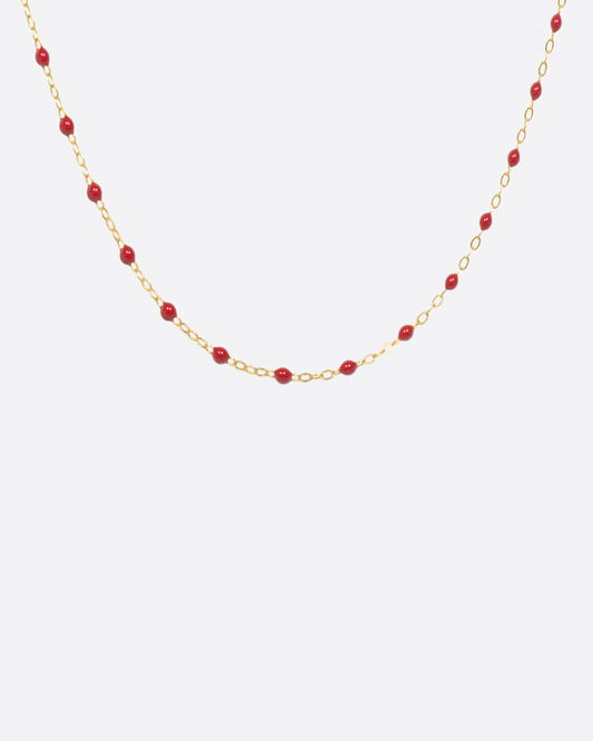 A yellow gold cable chain necklace with droplets of red resin. Shown from the front.