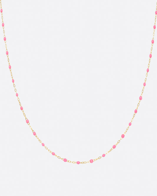 A yellow gold cable chain necklace with droplets of pink resin. Shown from the front.