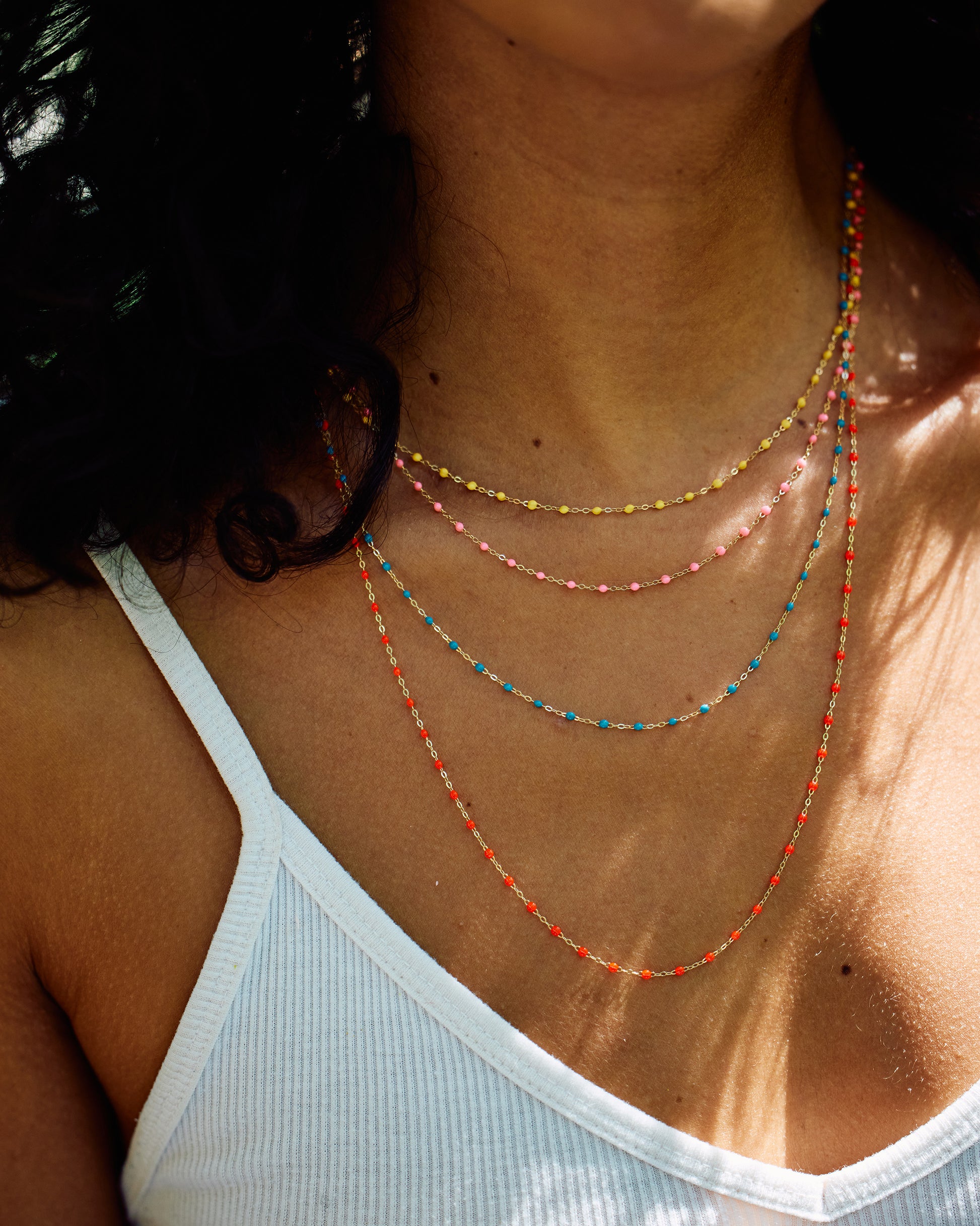 Four yellow gold cable chain necklaces shown from the front layered on a person. The bottom one has coral resin droplets, the next has turquoise resin droplets, the next pink resin droplets, the top yellow resin droplets.