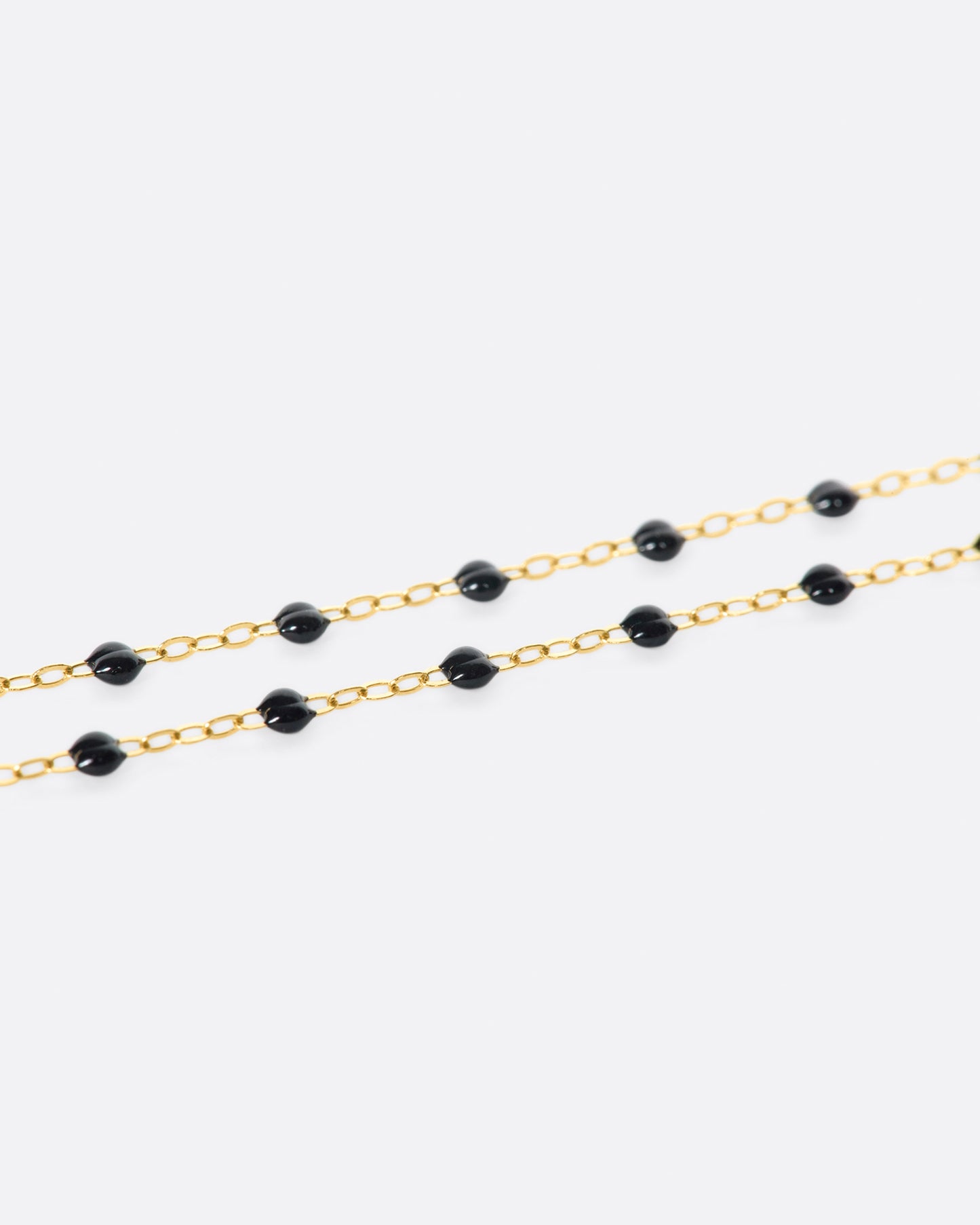 A close up view of a yellow gold cable chain necklace with black resin droplets. Shown from the side.