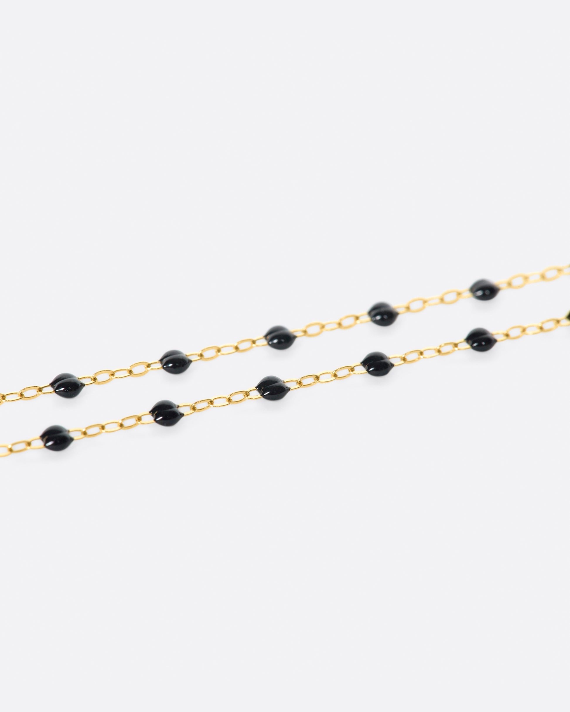 A close up view of a yellow gold cable chain necklace with black resin droplets. Shown from the side.