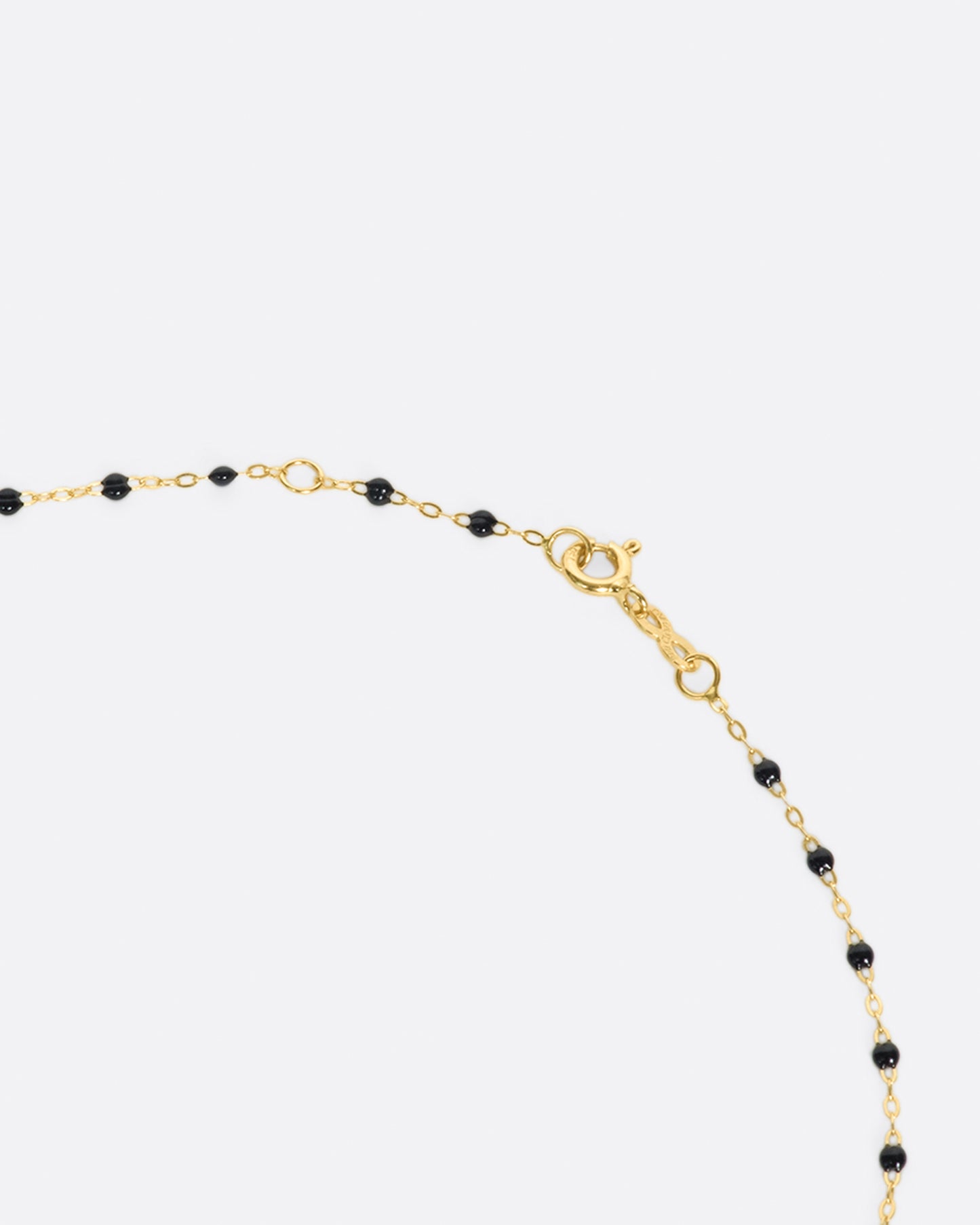 A close up view of a yellow gold cable chain necklace with black resin droplets and its clasp. Shown from the side.