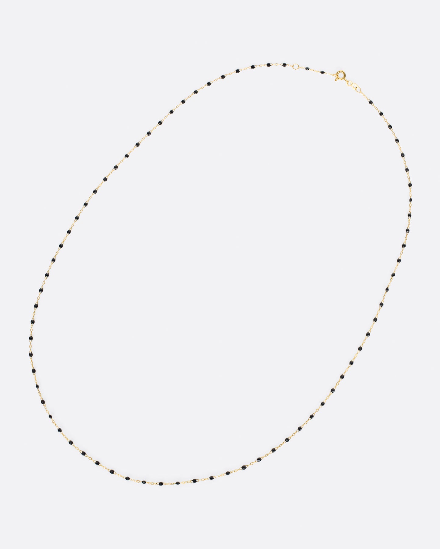 A yellow gold cable chain necklace with droplets of black resin. Shown clasped lying flat diagonally from the front.