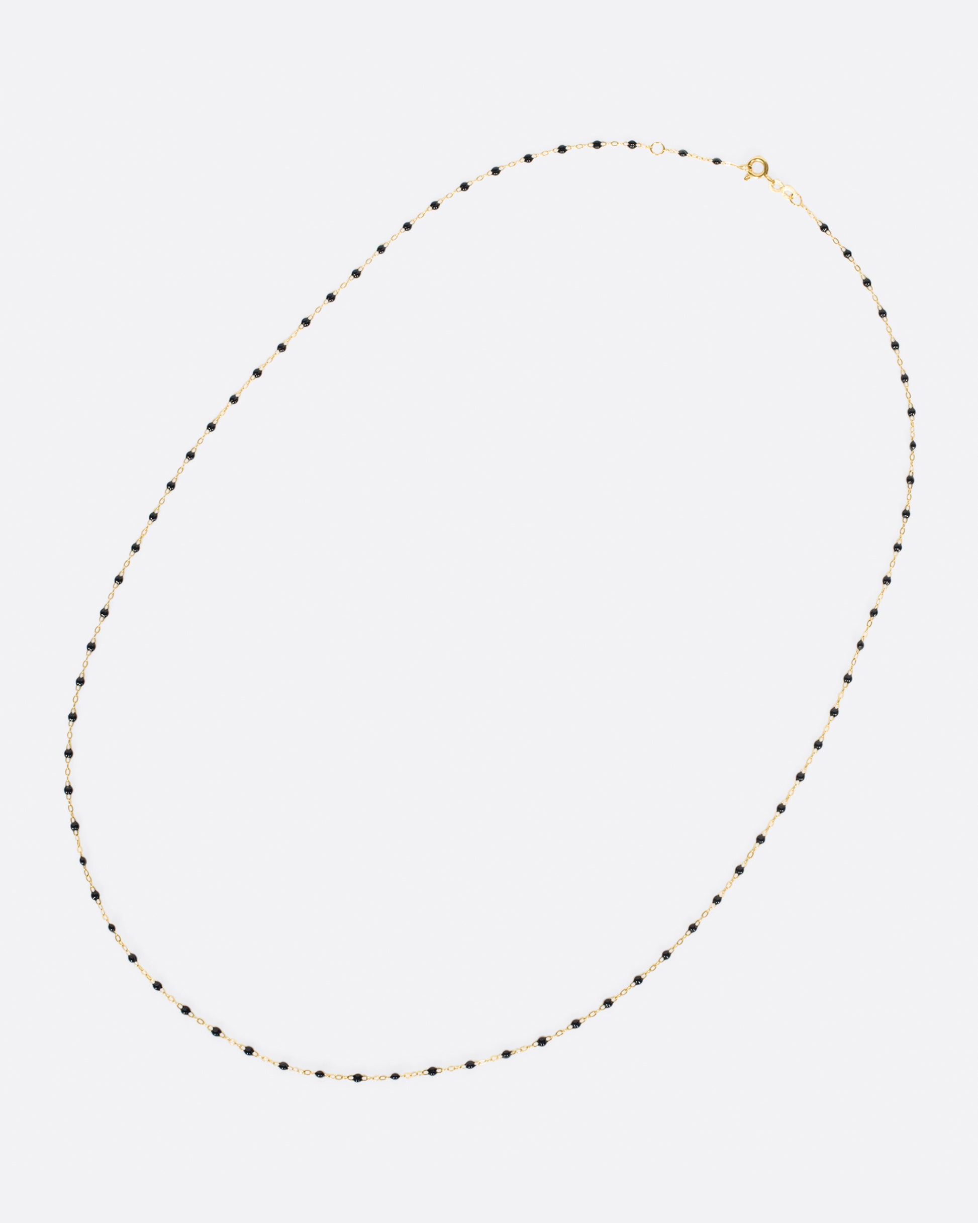 A yellow gold cable chain necklace with droplets of black resin. Shown clasped lying flat diagonally from the front.