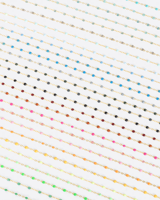 A close up view of yellow gold cable chains with multicolored resin droplets. Shown diagonally.