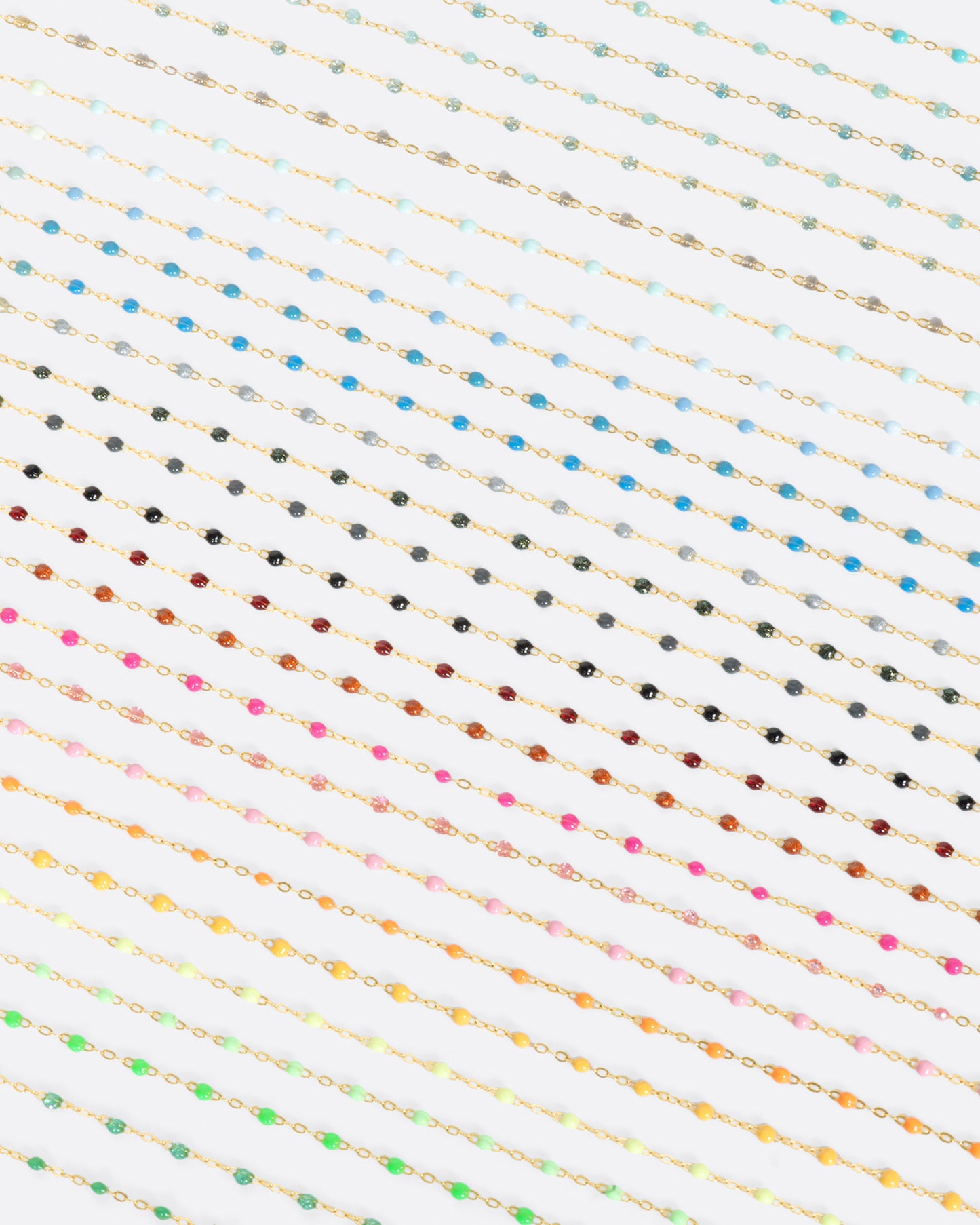 A close up view of yellow gold cable chain necklaces with multicolored resin droplets. Shown diagonally.