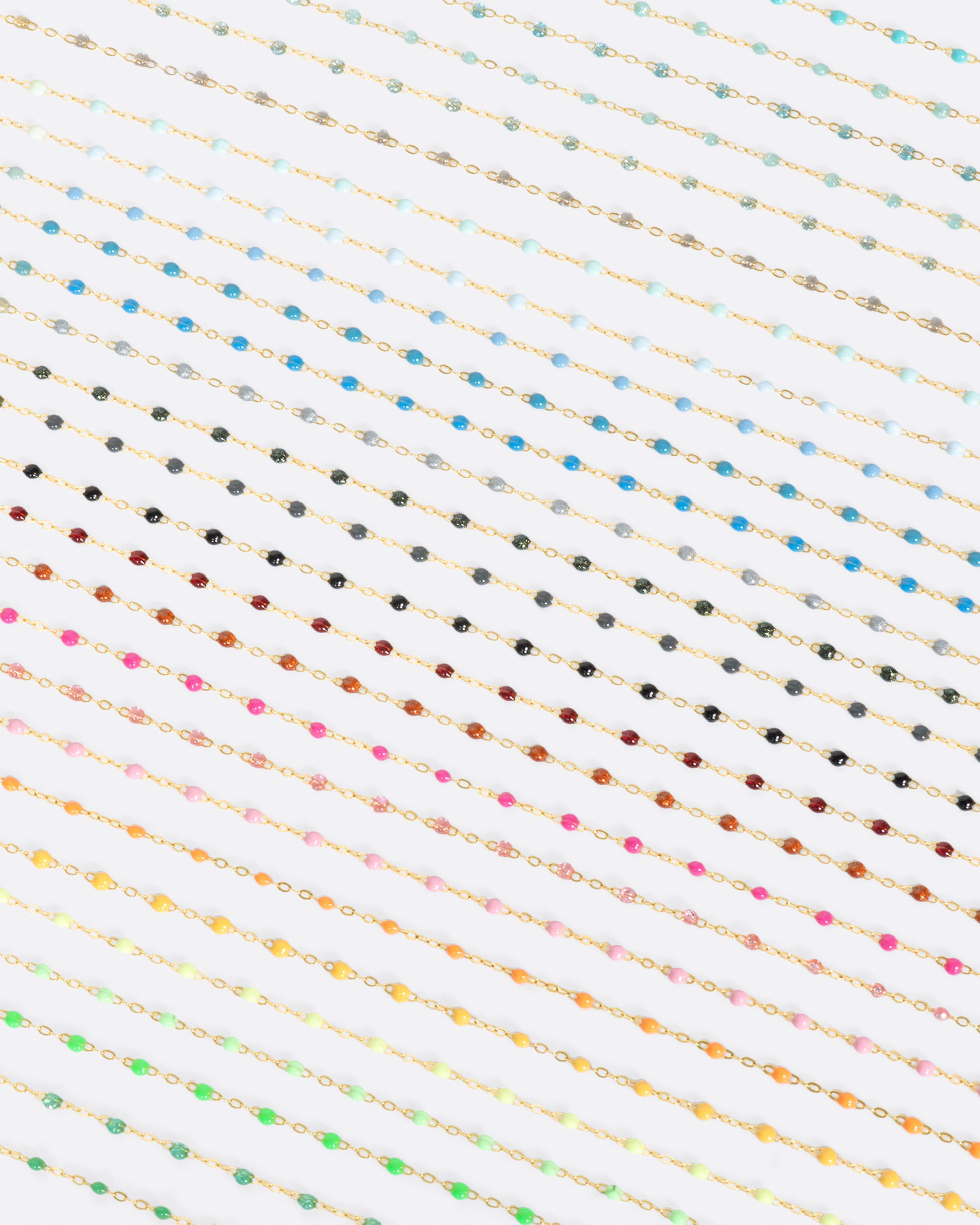 A close up view of yellow gold cable chain necklaces with multicolored resin droplets. Shown diagonally.