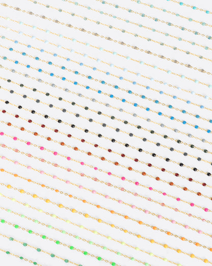 A close up view of yellow gold cable chain necklaces with multicolored resin droplets. Shown diagonally.