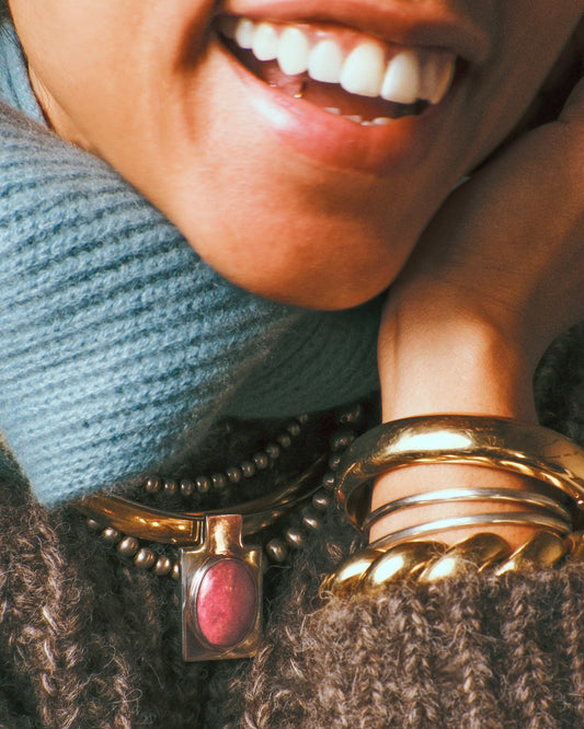 A sterling silver rectangular pendant with an oval pink stone cabochon shown styled around a neck paired with a gold collar and beaded silver necklace.
