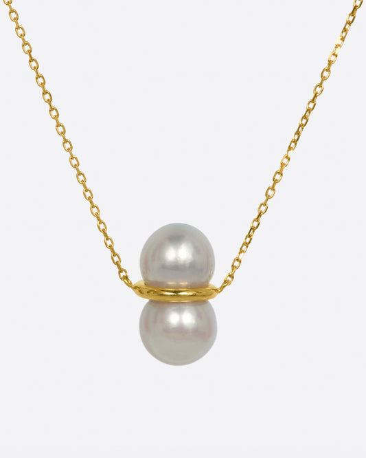 Two large pearls are paired vertically with a gold setting, and attached to a gold necklace.