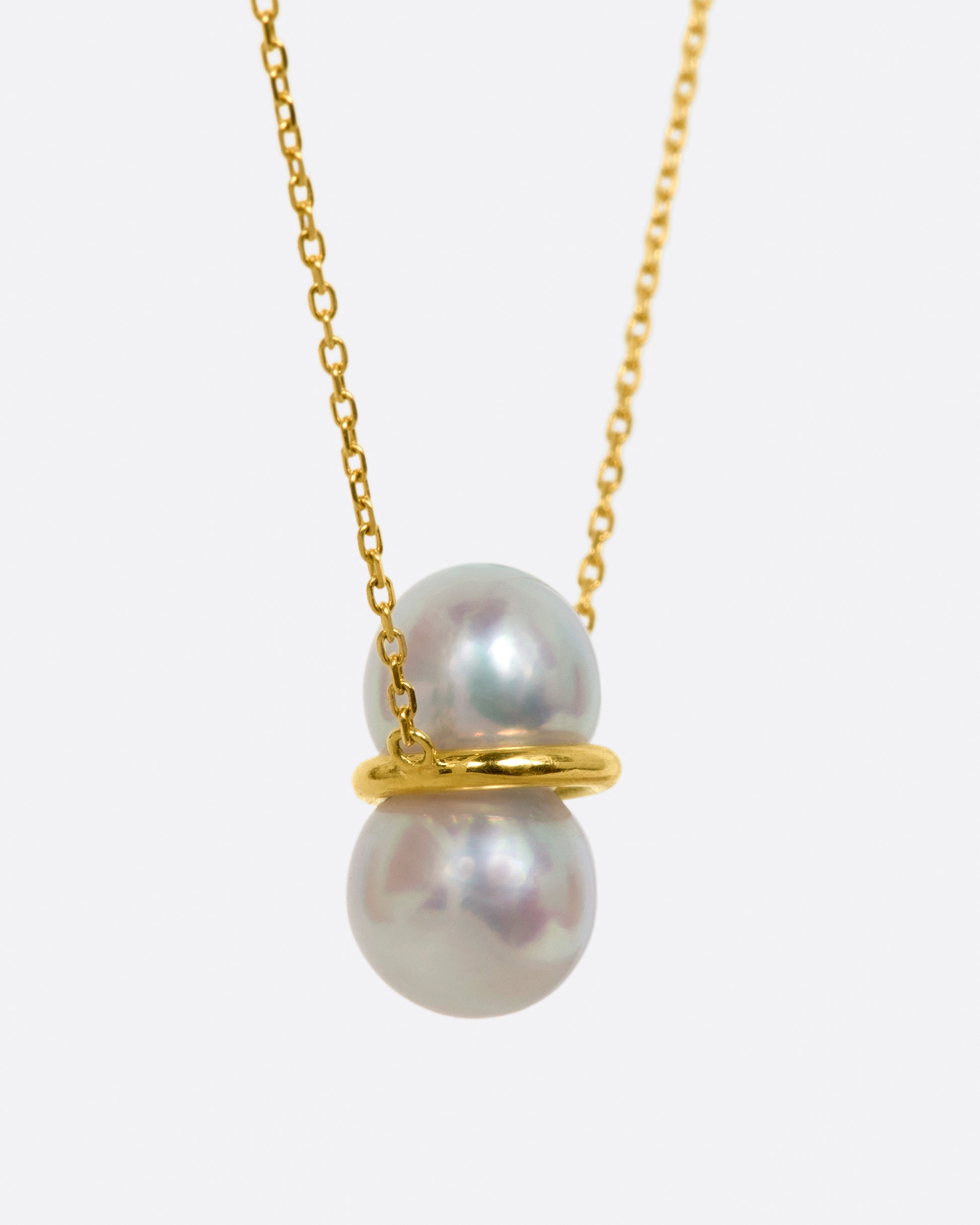 Two large pearls are paired vertically with a gold setting, and attached to a gold necklace. View from the side.