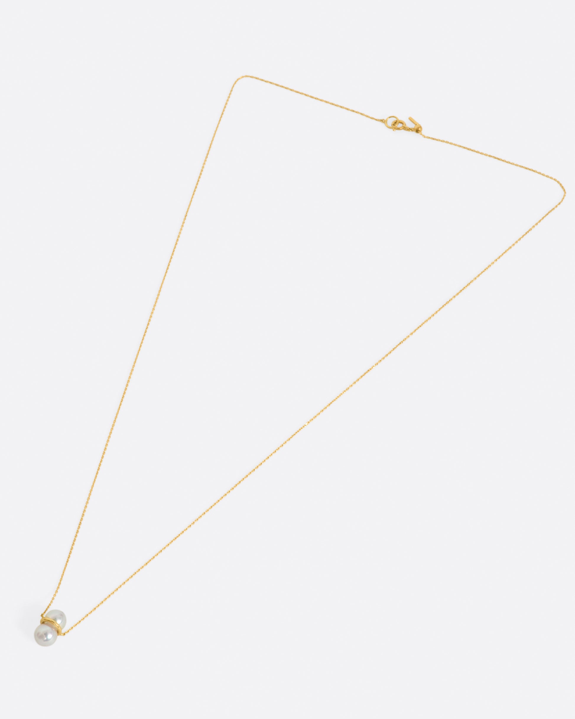 Two large pearls are paired vertically with a gold setting, and attached to a gold necklace. View from above, laying flat.