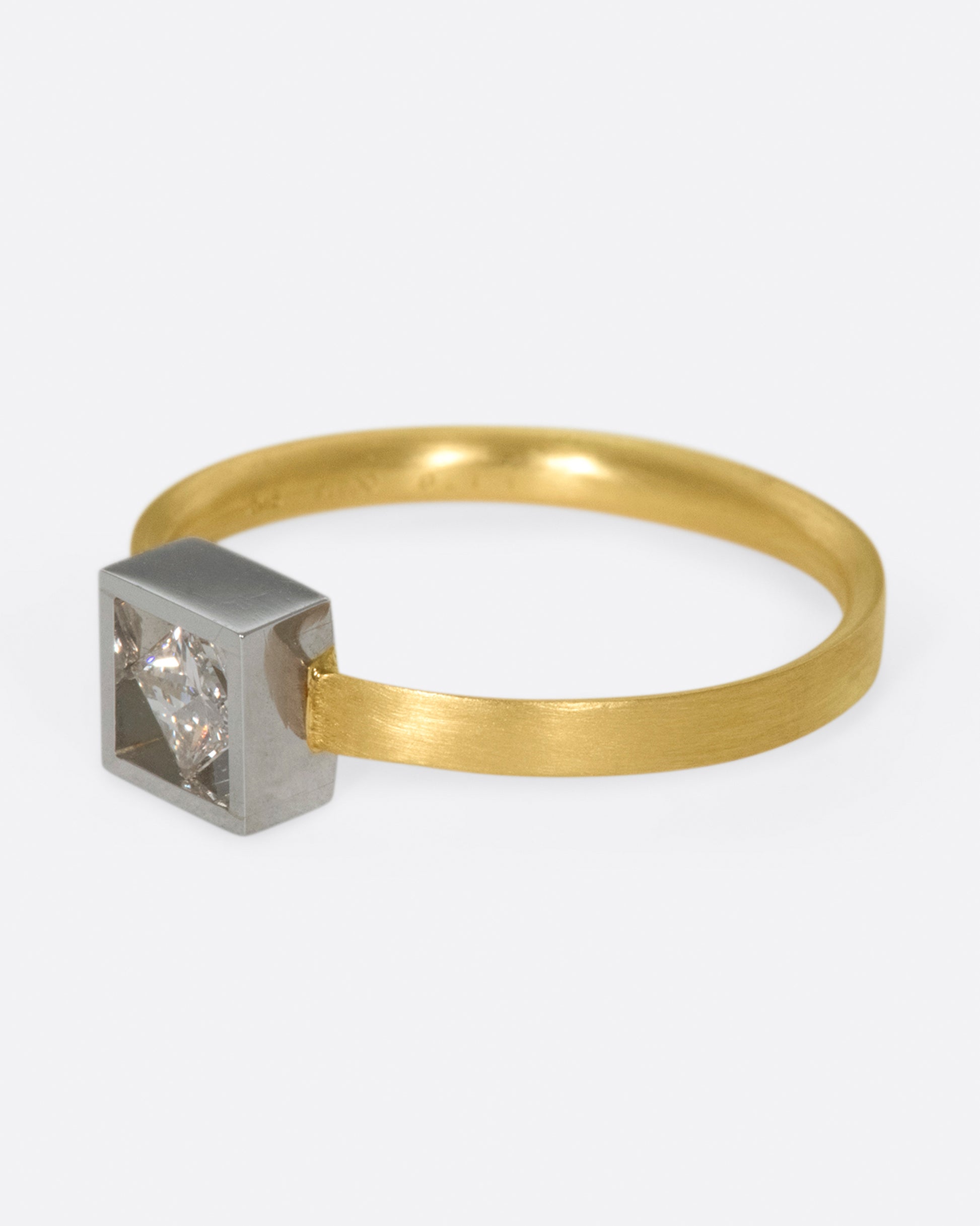 A geometric solitaire ring with a princess cut diamond set on its side in a platinum setting on a yellow gold band.