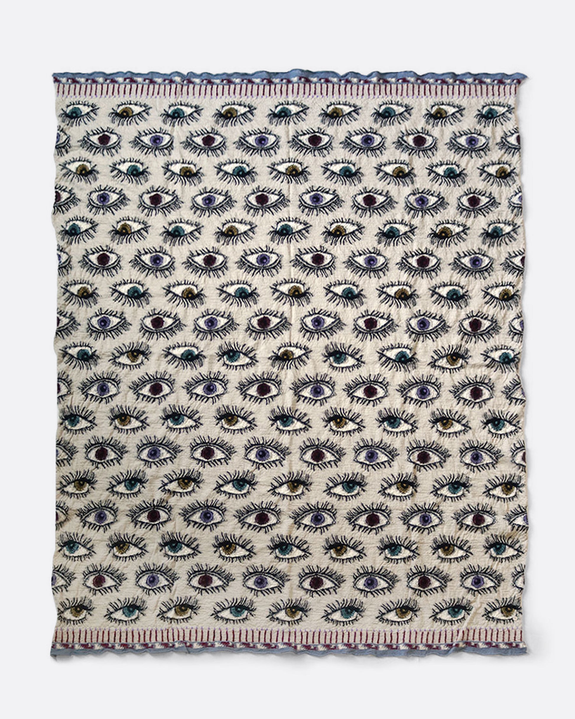 A cream colored compressed wool blanket from with an all- over eye pattern. Shown open lying flat.