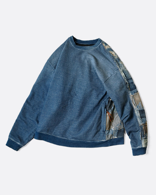 A crewneck sweatshirt with an indigo dyed cotton front and a distressed Boro patchwork on the reverse. Shown from the side.
