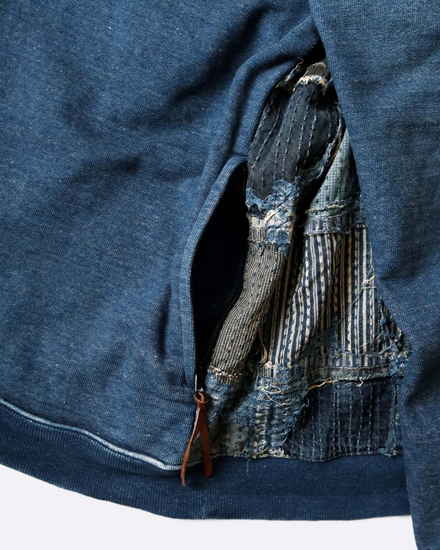 A close up of the pocket detail of a crewneck sweatshirt with an indigo dyed cotton front and a distressed Boro patchwork on the reverse. 