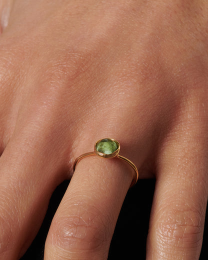 A yellow gold ring with a green tourmaline cabochon, shown on a hand.